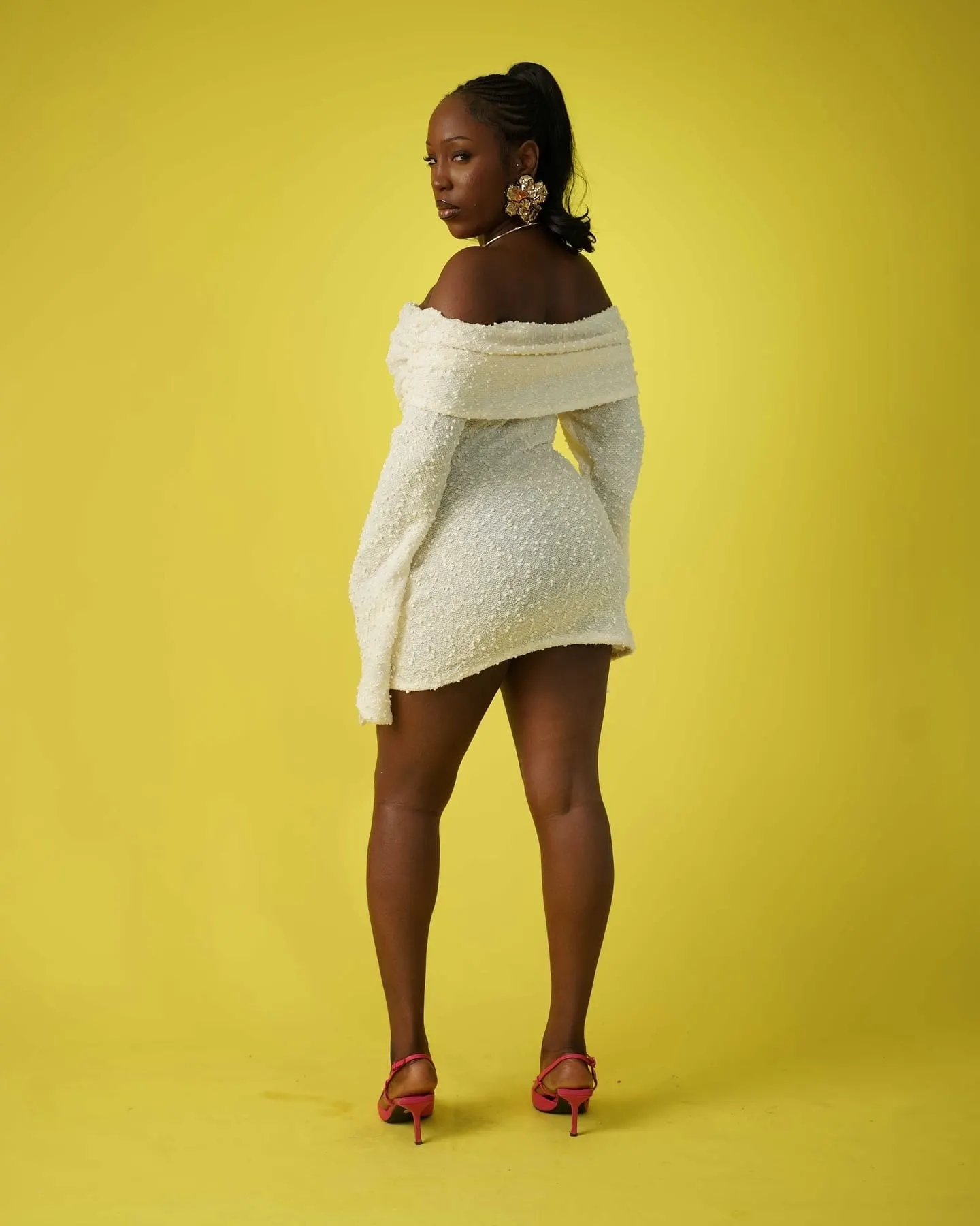 Model seen from behind in a white off-shoulder mini dress, looking back over her shoulder.