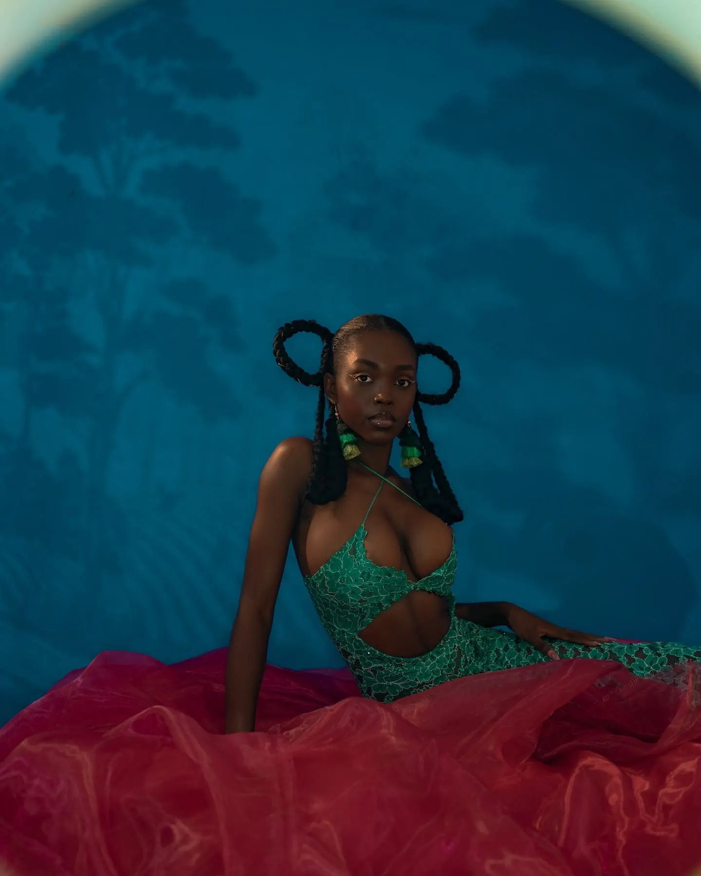 Uyi reclines on crimson tulle in the green lace gown, braided loops crowning her steady gaze.