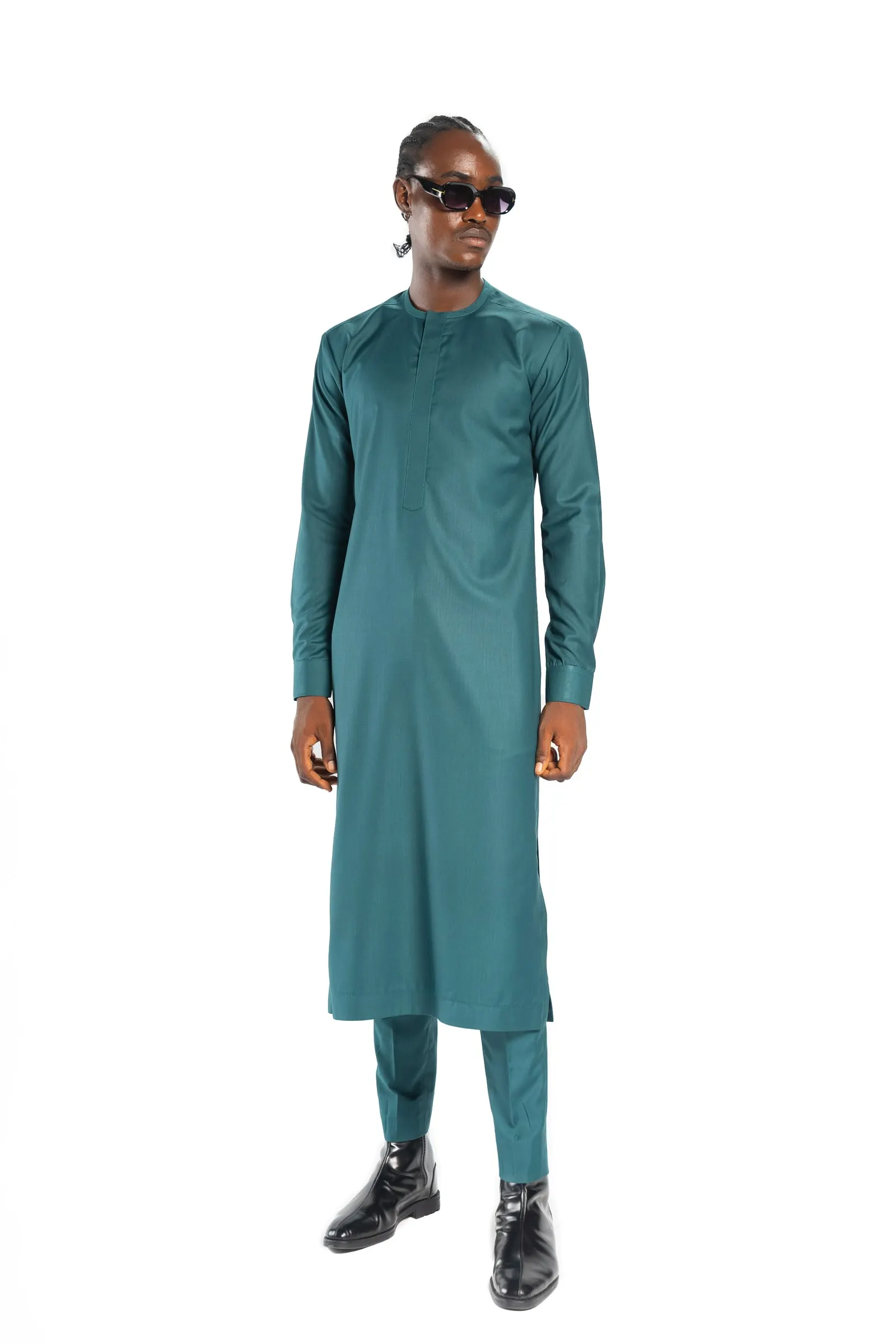 Model in sunglasses and a long teal kaftan with matching trousers stands front-on against a white studio background.
