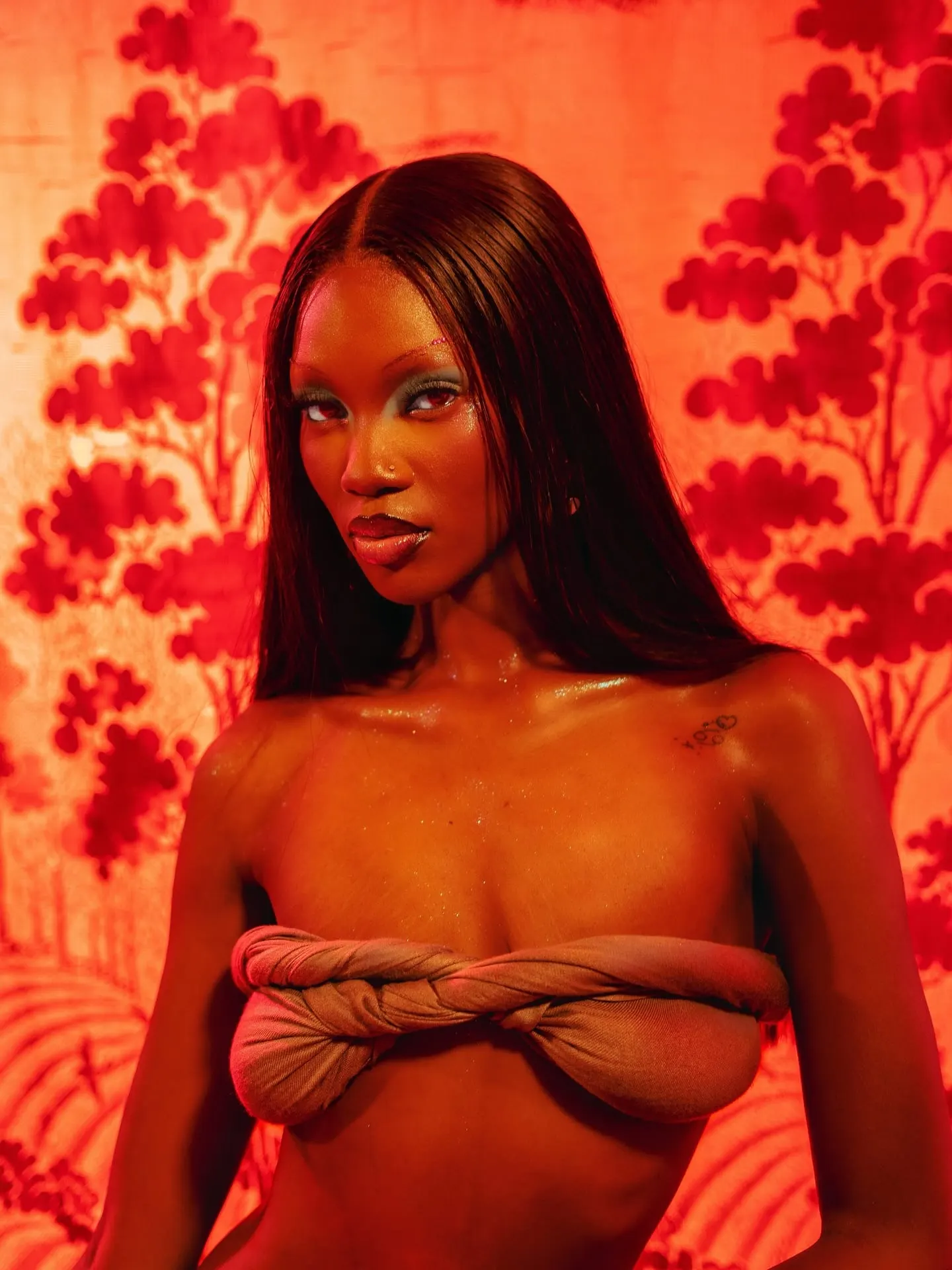 Model gazes intently at the camera in a twisted taupe wrap top, bathed in deep red light.