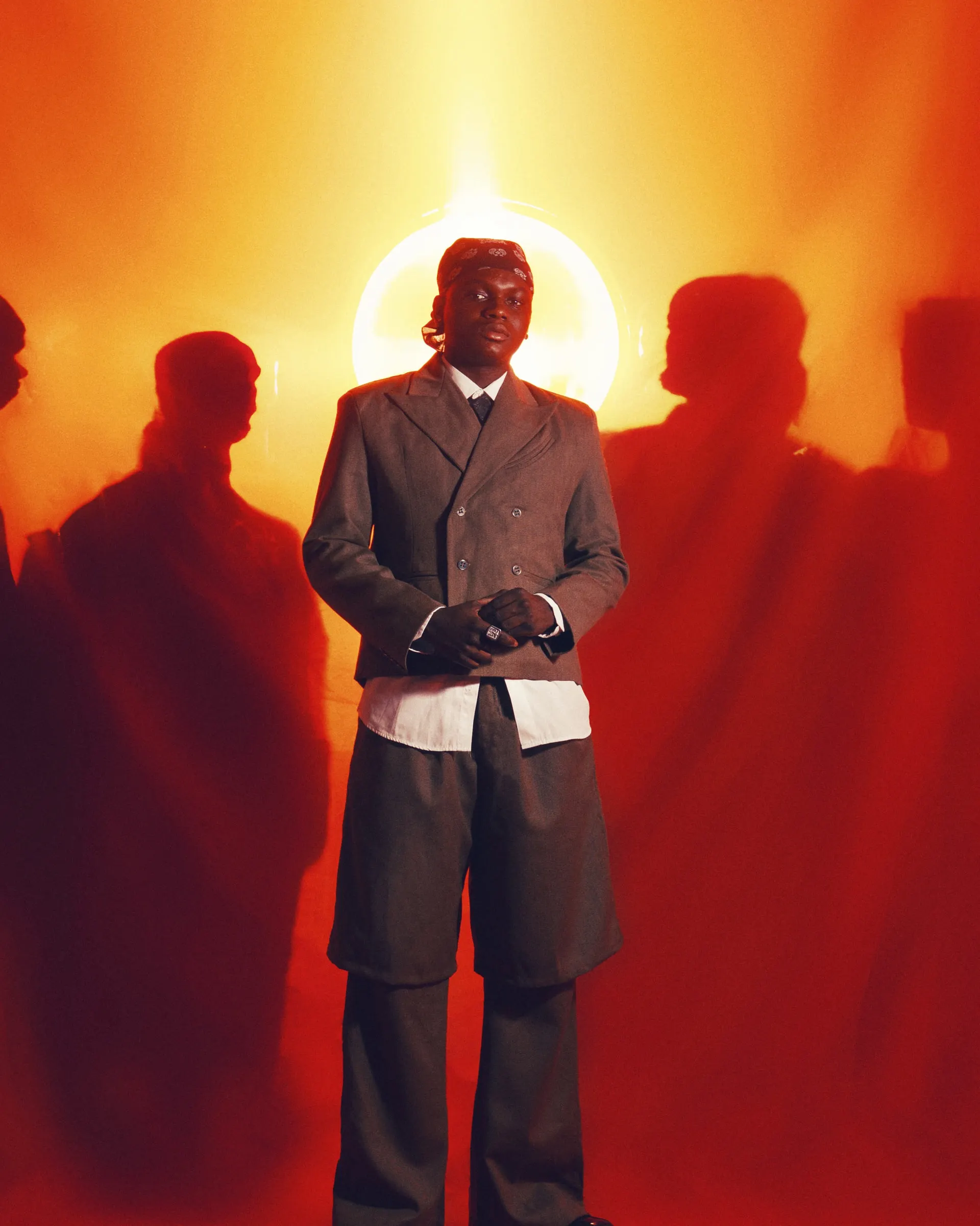 Orange magazine cover — Ayo Maff in a grey double-breasted suit standing before a glowing halo, shadowy figures gathered in the red-orange haze, titled 'The Prince of the Street'.