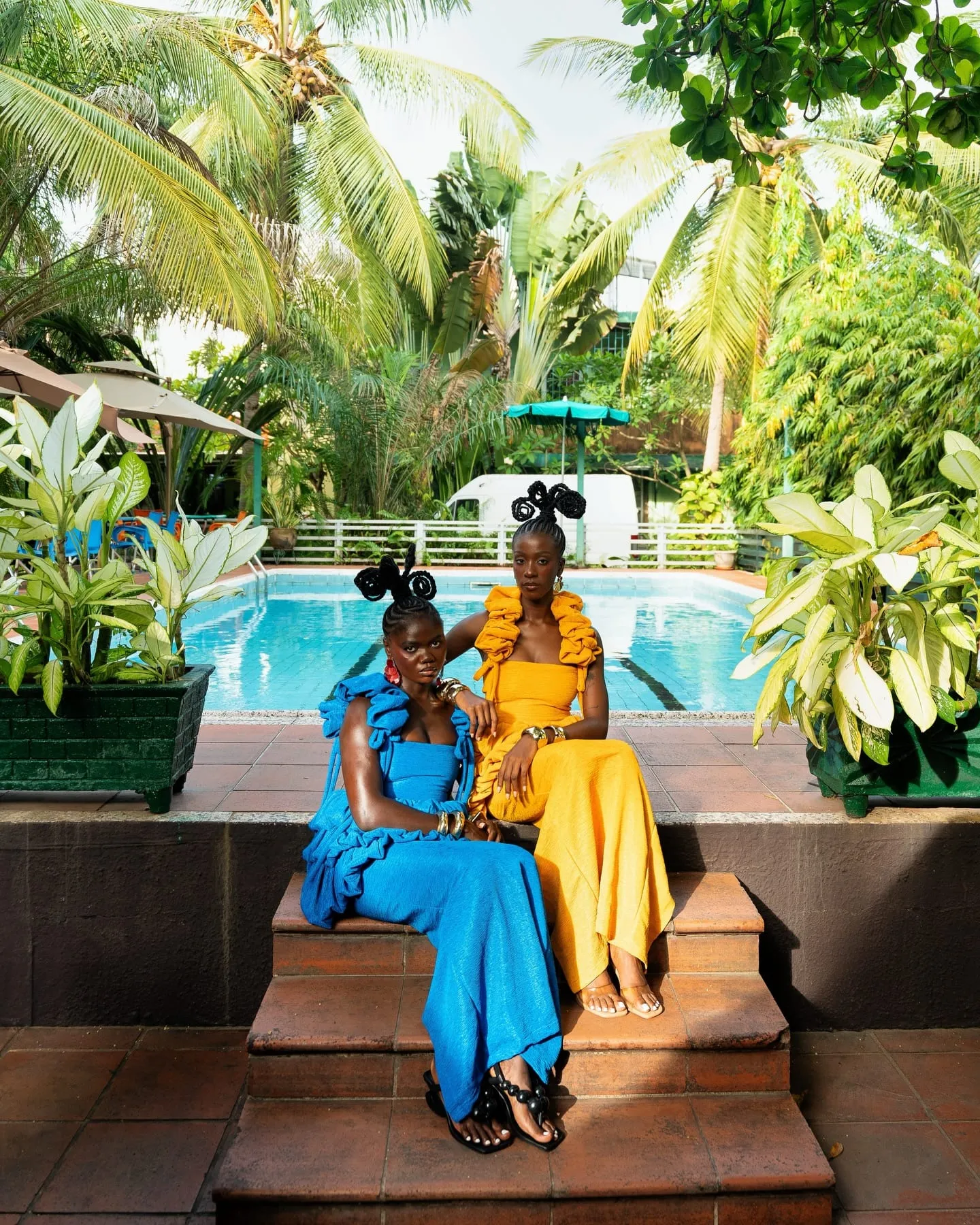 Poolside scene — a figure in black beside turquoise water, palms rising behind.