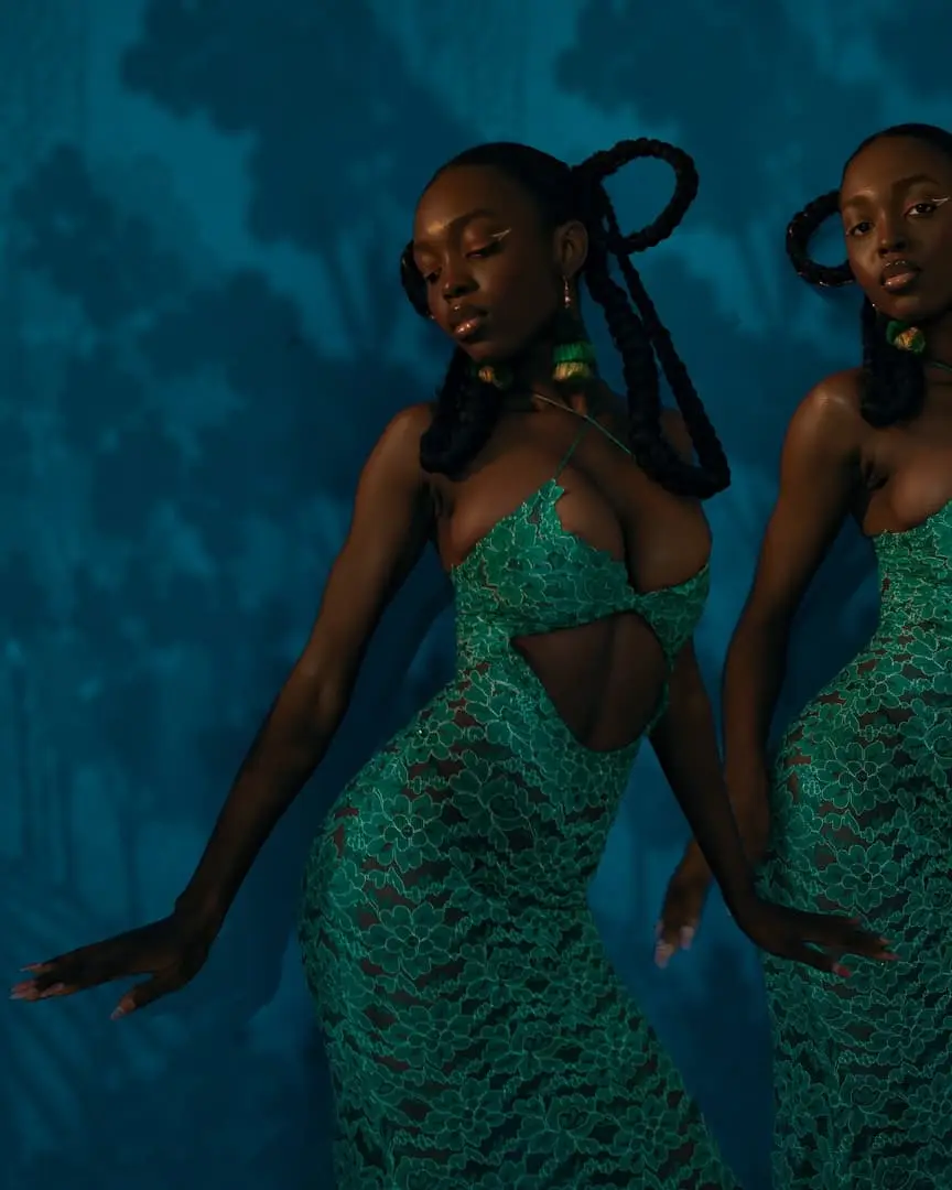 Two dancers in green lace gowns with looped braids move against a blue forest-shadow backdrop.
