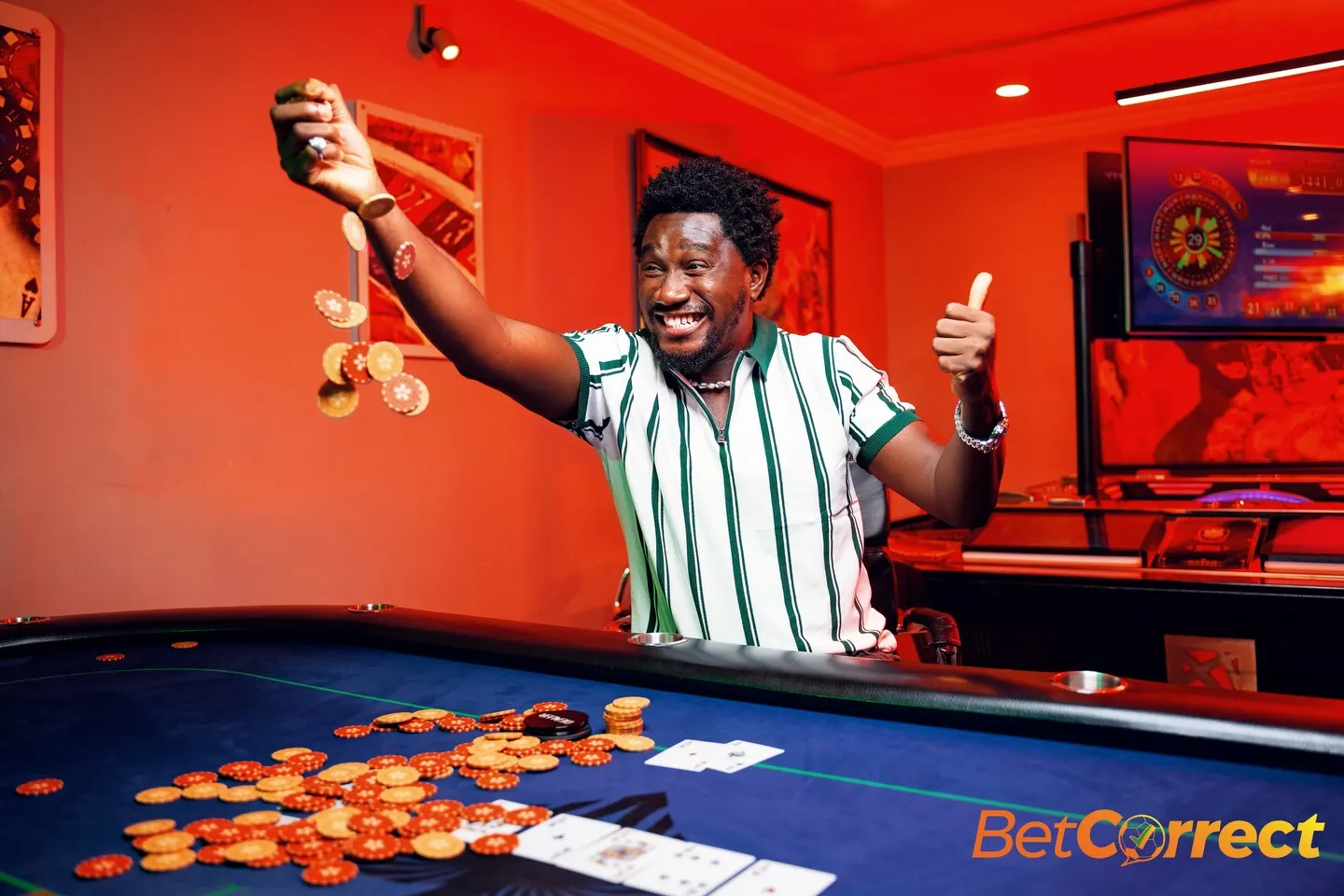 Comedian in a green-and-white striped shirt throws both arms up in celebration, coins falling from one fist, over a chip-strewn blue poker table in a red-lit casino.