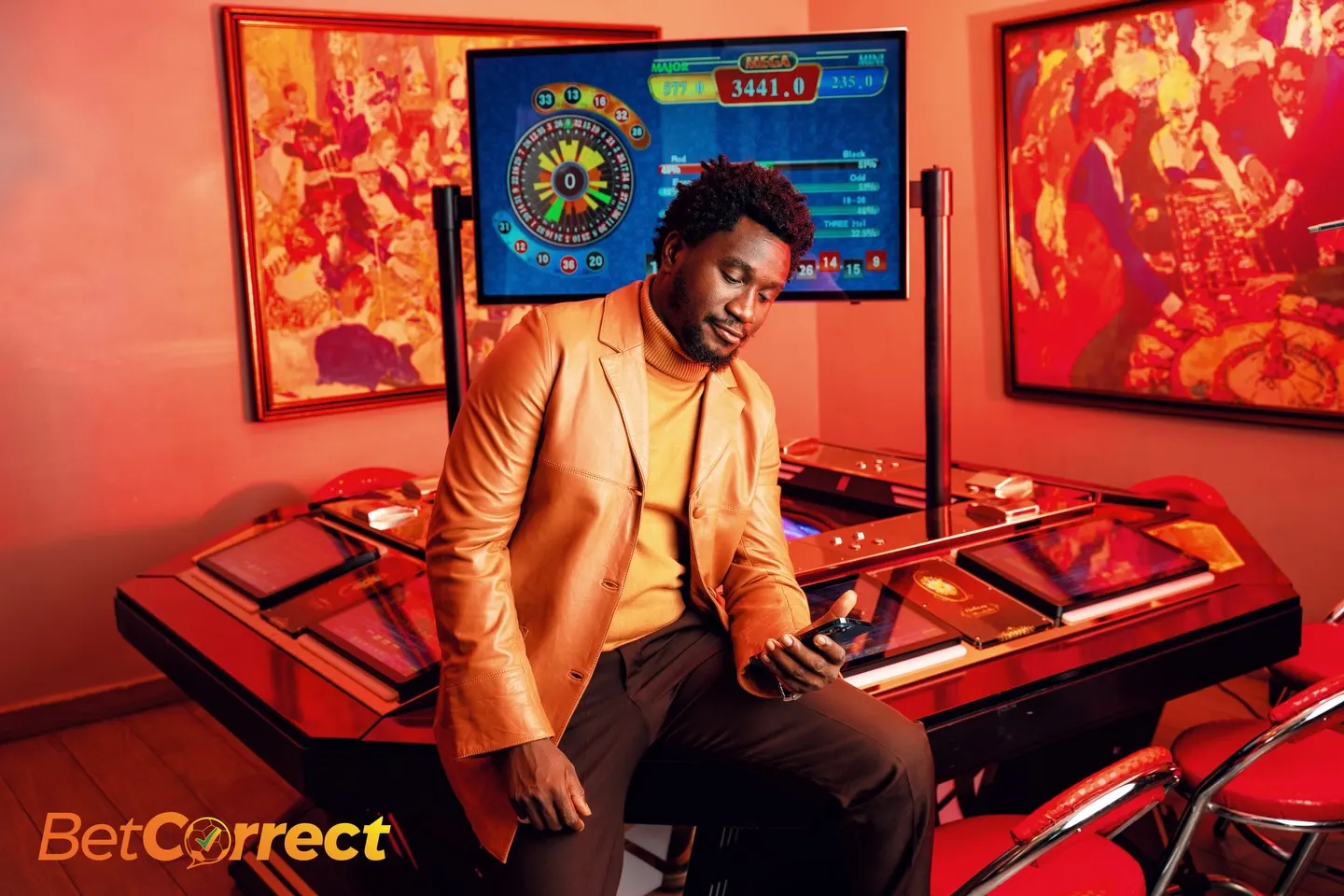 Man in a tan leather blazer over a marigold turtleneck sits on the edge of a gaming table checking his phone, framed by red-toned casino paintings and a roulette screen.