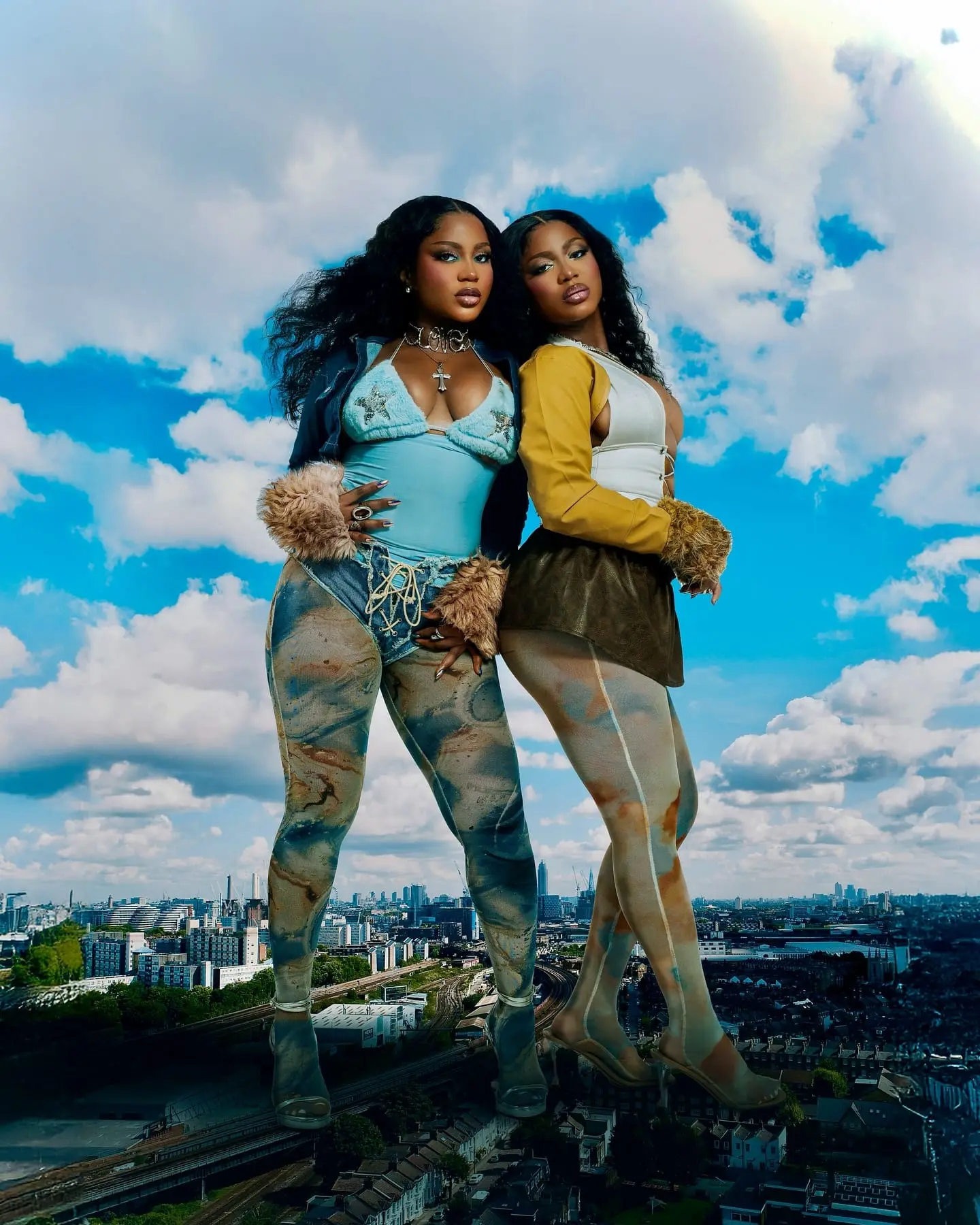 Two models in Y2K-style fur-cuffed outfits tower like giants over a city skyline beneath blue skies.